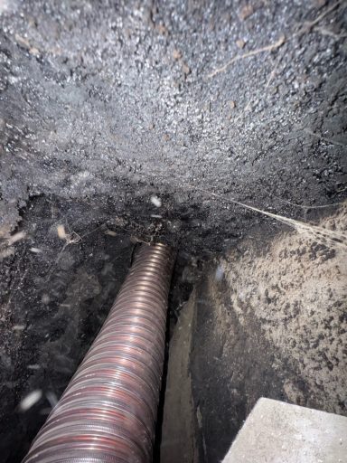 A view of a drainage pipe emerging from the ground, surrounded by soil.
